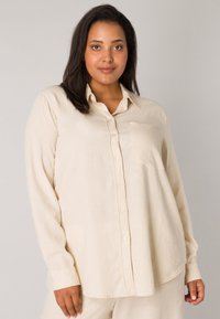 Cream-colored long-sleeve button-up shirt with a front pocket. Made from textured fabric, features a classic collar and straight hem.