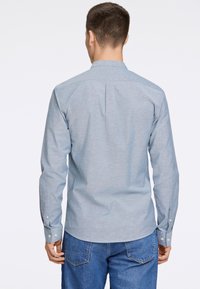 Camisa de manga larga azul claro con cuello, puños abotonados, una costura en la parte trasera y una tela texturizada, combinada con unos pantalones vaqueros azules.