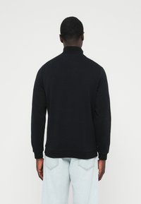 Zwarte trui met hoge kraag, geribbelde manchetten en zoom. Gemaakt van een gladde stof, minimale details en een comfortabele pasvorm.