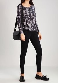 Långärmad tröja med svart och grå abstrakt mönster, kombinerad med svarta leggings och glansiga loafers. En svart axelväska fulländar looken.