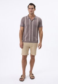 Polo à manches courtes en mauve poussiéreux avec des rayures verticales blanches, associé à un short beige et des sandales marron, avec un design à patte de boutonnage.