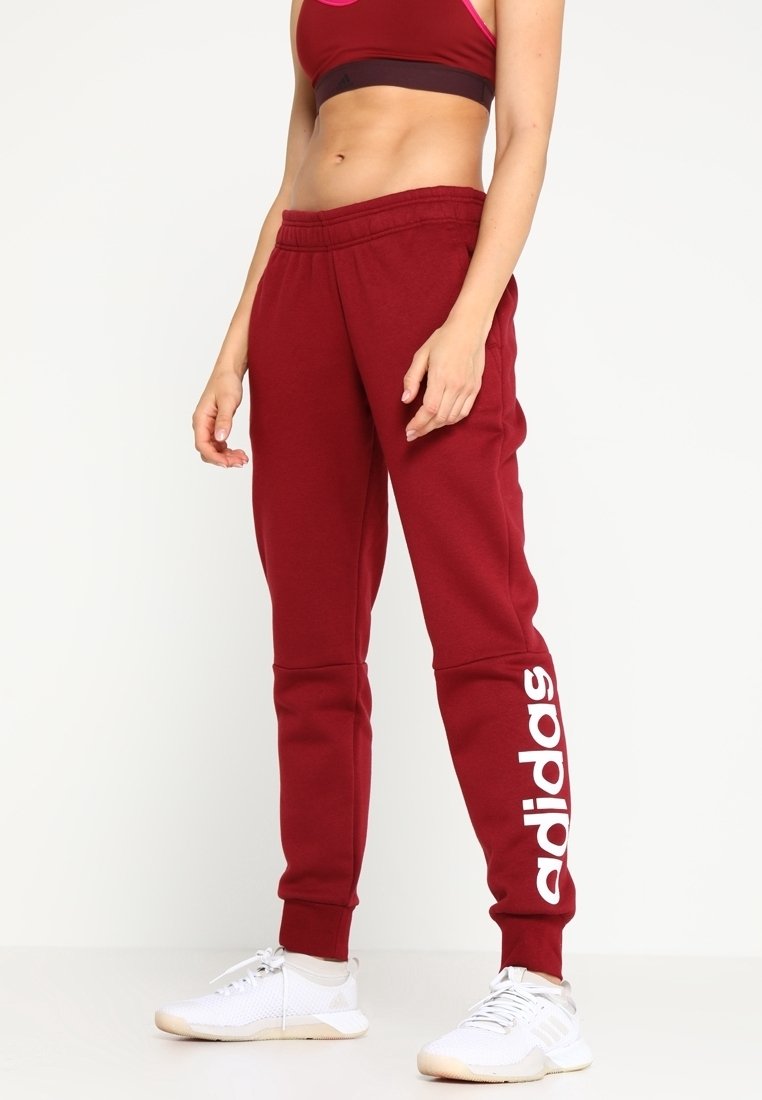 Pantalones de chándal burdeos hechos de una tela suave con cintura elástica y puños. Presenta un gran logo blanco de "adidas" en el lado izquierdo.