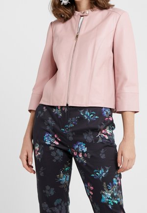 Lys pink læderjakke med lynlås, trykknapkrave og trekvartærmer, parret med bukser med mørkt blomsterprint.