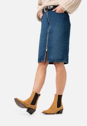 Jupe en denim droite avec une fermeture éclair à l'avant, de couleur bleu foncé, assortie à des bottes chelsea en suède beige avec des panneaux élastiques sur les côtés et un talon bloc.