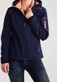 Marineblaues Softshell-Jacket mit einem hellrosa Innenfutter, mit Reißverschlüssen versehenen Taschen und kontrastierenden orangefarbenen Hardware-Details. Verstellbare Kapuze, taillierte Passform.