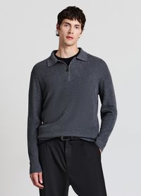 Grauer gestrickter Pullover mit Kragen und einem halbhohen Reißverschluss. Verfügt über eine gerippte Textur und lange Ärmel. Wird über einer schwarzen Hose getragen.