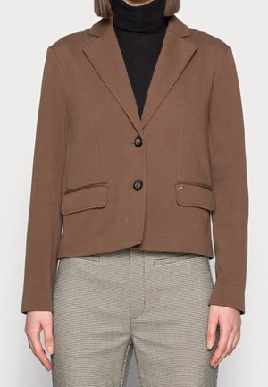 Blazer marrón entallado con solapas con muesca, dos botones y bolsillos con solapa, combinado con un jersey de cuello alto negro y pantalones estampados.