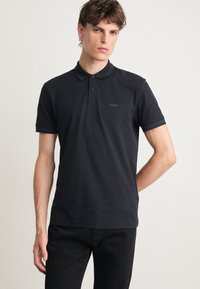 Μαύρο πόλο μπλουζάκι φτιαγμένο από βαμβάκι με κλασικό γιακά, τρία κουμπιά και κοντά μανίκια. Διαθέτει διακριτική σήμανση στο στήθος.