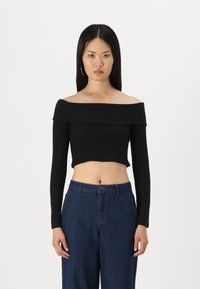 Juodas off-the-shoulder vamzdinis trumpas megztinis ilgomis rankovėmis. Pasižymi prigludusia forma ir lygia tekstūra. Derinamas su aukštu juosmeniu mėlynomis džinsinėmis kelnėmis.