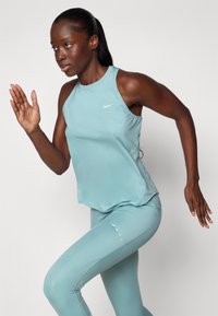 Lichtblauwe sportieve tanktop en leggings met een strakke pasvorm. De stof lijkt glad te zijn, met subtiele reflecterende accenten en minimale merkvermelding.