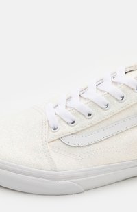 Baskets à paillettes blanches avec une texture lisse, des lacets blancs et un accent en cuir sur le côté, présentant un design basse silhouette.