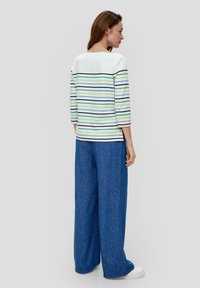 Gestreiftes Langarmshirt in Weiß, Blau, Grün und Schwarz, kombiniert mit weit geschnittenen blauen Denim-Hosen. Der Stoff wirkt weich und hat eine lässige Passform.