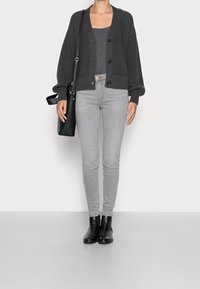 Šedý pletený kardigan s velkými knoflíky, doplněný šedým tílkem a světlými šedými úzkými džínami. Černé kotníkové boty a černá taška.