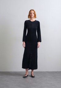 Black, long-sleeved dress featuring a fitted silhouette and a ruffled detail at the hem. Made from a smooth, textured fabric.