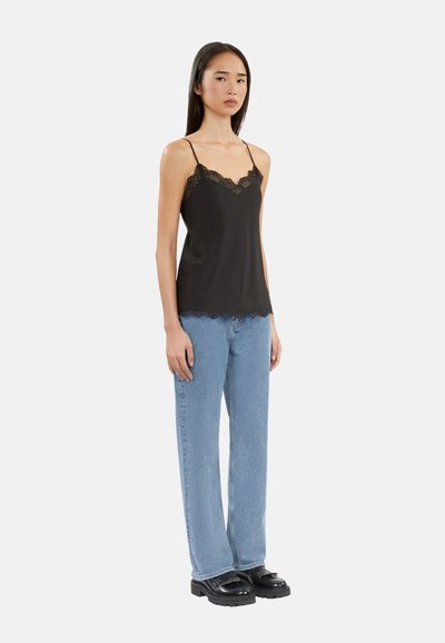 Svart satin cami med blondekant og justerbare stropper, kombinert med lyseblå rette jeans og svarte platåsko.