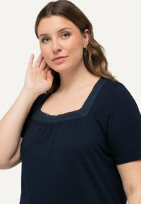 Námořnická modrá halenka s krátkým rukávem a čtvercovým výstřihem lemovaným krajkou, se volným střihem a měkkou texturou.