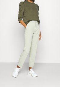 Olivgrön tröja med puffärmar och en chevron-söm, tillsammans med ljusgröna skräddarsydda byxor och vita chunky sneakers.