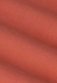 Tissu doux et lisse de couleur terracotta chaude avec de subtils plis et une texture de tissage fine.