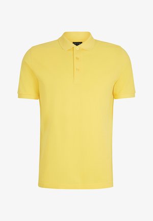 Żółta koszulka polo z kołnierzykiem, zestawiona z szarymi dresami. Model nosi białe trampki. Materiał wydaje się gładki, a styl jest casualowy i swobodny.