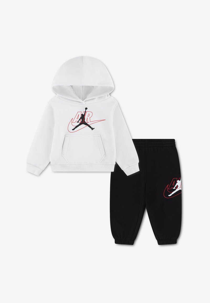 Sweat à capuche blanc avec logo Air Jordan noir et rouge, associé à un pantalon de jogging noir à taille élastique avec un logo assorti sur la jambe.