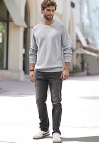 Grauer Strickpullover mit geripptem Muster, kombiniert mit dunkelgrauen Jeans und weißen Sneakers mit schwarzen Akzentstreifen. Steht im Freien.