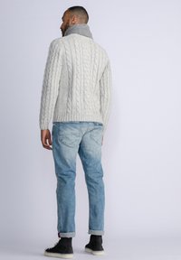 Suéter de punto con trenzado en gris claro y cuello alto, combinado con jeans azul desgastado y botas negras hasta el tobillo. El suéter presenta un detalle texturizado.