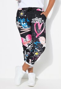 Pantalons de jogging noirs avec un imprimé graffiti en rose, bleu et blanc. Comprend une taille élastique et des poches latérales, avec un design de jambe fuselée.