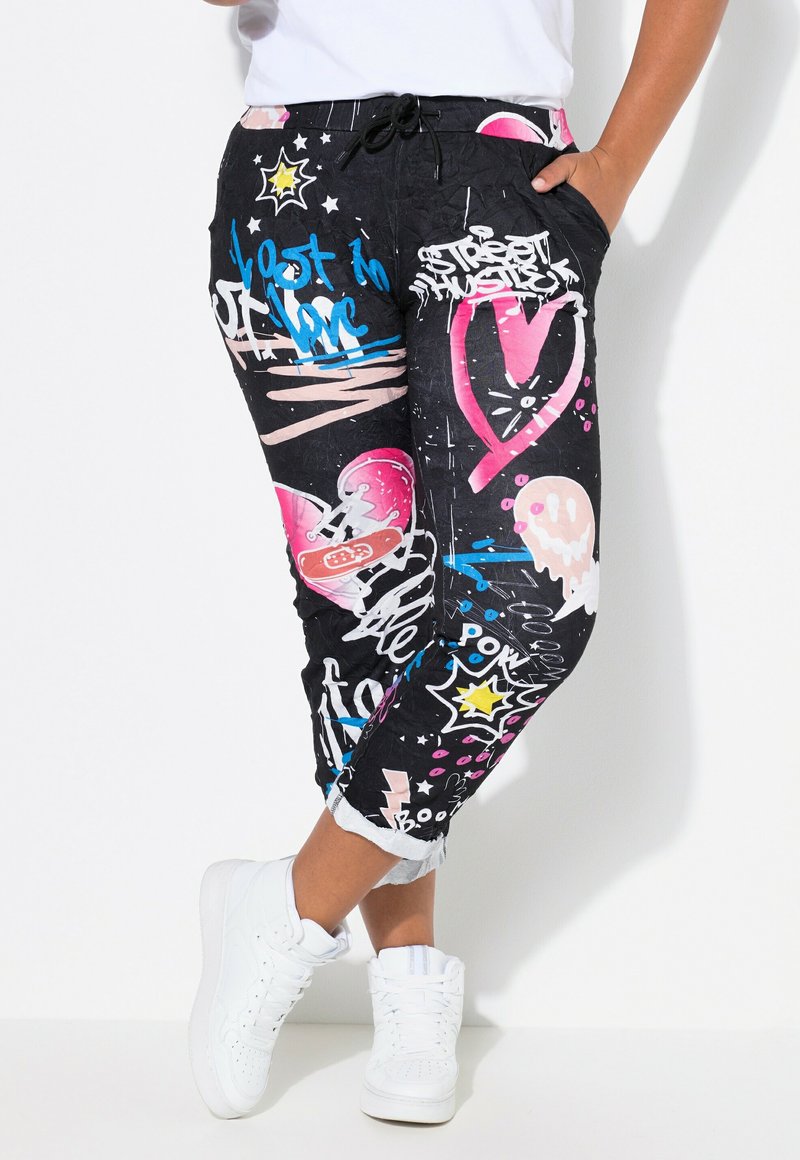 Pantalons de jogging noirs avec un imprimé graffiti en rose, bleu et blanc. Comprend une taille élastique et des poches latérales, avec un design de jambe fuselée.