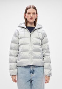 Svijetlosiva puf jakna s kapuljačom, zatvaranjem na patentni zatvarač i elastičnim manžetama; ima kvadratne šavove za izolaciju i skraćeni dizajn.