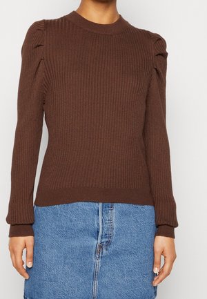 Brązowy sweter z prążkowanej dzianiny z okrągłym dekoltem i bufkami na ramionach. Długie rękawy z dopasowanymi mankietami, w połączeniu z dżinsową spódnicą.