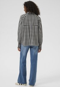 Plaid shirt with black, white, and gray colors; long sleeves; back pleat detail; paired with blue flared jeans and cream sneakers.