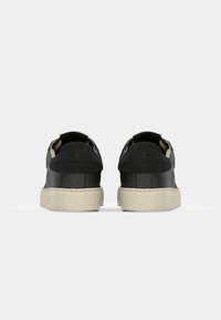Sneakers in pelle nera con finitura testurizzata, caratterizzati da una suola beige chiaro a contrasto e un marchio discreto sul tallone. Design con punta arrotondata.