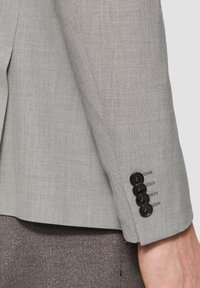 Szary blazer w wzory z teksturowanym wykończeniem. Posiada klapę w kształcie notcha oraz cztery czarne guziki na mankiecie, z dopasowanym krojem rękawów.