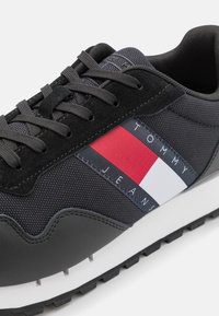 Sneaker atletico nero con una tomaia in tessuto testurizzato, dettagli in pelle scamosciata e una striscia del logo in rosso, bianco e blu. Suola in gomma.