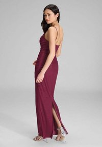 Bordeaux Abendkleid mit taillierter Silhouette, Spaghettiträgern, Raffungen und einem Seitenschlitz, kombiniert mit klaren Absatzsandalen.