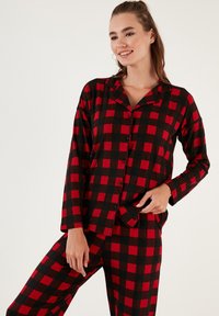 Conjunto de pijama a cuadros rojos y negros hecho de tela suave; cuenta con mangas largas, una camisa con cuello y pantalones con cintura elástica y detalle de botones.