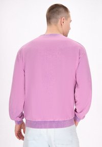 Pullover viola chiaro con polsini e orlo a costine. Texture liscia, vestibilità rilassata e design a collo rotondo. Vista posteriore con dettagli minimi.