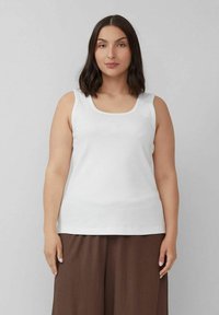 Weißes Tanktop, ärmellos, Rundhalsausschnitt, gerippte Textur, schlichtes Design. Kombiniert mit lockeren, braunen, strukturierten Hosen.