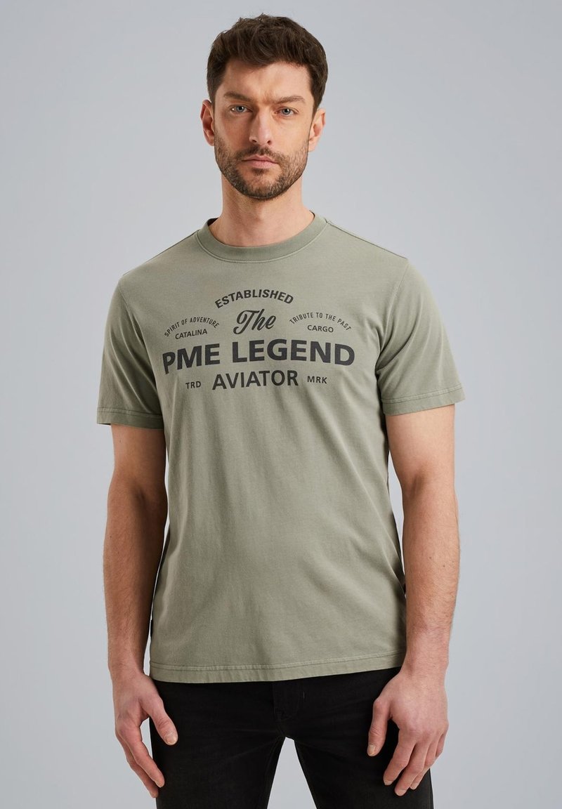 Camiseta de algodón verde oliva de mangas cortas y cuello redondo, con texto impreso en negro en una fuente en negrita en la parte frontal.