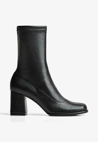 Botte mi-mollet en cuir noir avec un talon bloc, un bout carré arrondi et des détails de couture visibles le long de la couture supérieure et latérale.