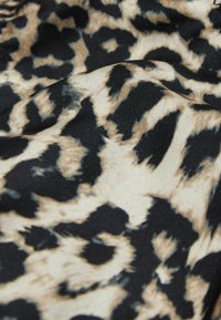 Leopardprint stof med en blanding af sort og beige farver, der viser en blød tekstur og et tydeligt dyremønster med glat fald.