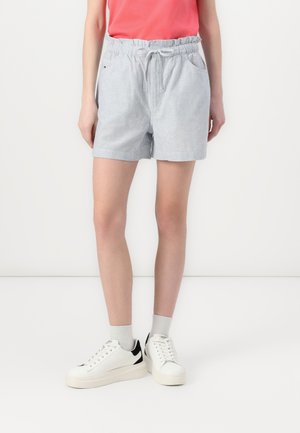 Pantaloni corti a righe azzurro chiaro con vita elastica e coulisse, dotati di tasche laterali. Abbbinati a sneaker bianche e calzini grigi.