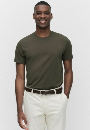 Mörkgrön bomulls t-shirt med rund halsringning, korta ärmar, i kombination med beige byxor och ett flätat brunt bälte. Slät textur.