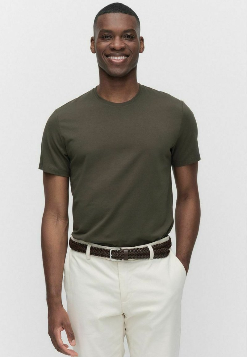 Mørkegrøn bomulds T-shirt med rund hals, korte ærmer, parret med beige bukser og et flettet brunt bælte. Glat tekstur.