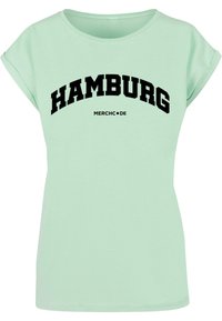 Mintgrønn t-skjorte med korte, rullede ermer og stor svart "HAMBURG"-trykk. Laget av myk stoff med en avslappet passform.