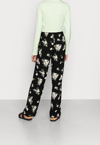 Mustat kukkakuviolliset housut, joissa valkoisia ja vaaleanpunaisia kukkia; väljä istuvuus ja pitkä pituus. Yhdistetty vaaleanvihreään, pitkähihaiseen crop-toppiin.