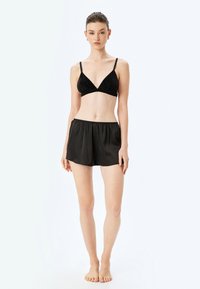 Top de bikini negro con un diseño texturizado, forma triangular y tirantes finos, combinado con pantalones cortos negros, ligeros y elásticos.