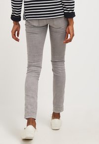 Jeans gris ajustados con una textura suave, silueta ceñida y detalles de costura sutiles. Combinados con zapatillas blancas.