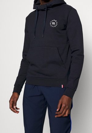 Navy hoodie with a front pocket, drawstring hood, and circular white graphic. Features elasticized cuffs and hem, made from soft material.