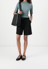 Czarne szorty o dopasowanym kroju, w połączeniu z jasnoniebieskim dopasowanym topem i czarną skórzaną torbą na ramię. Czarne lakierowane buty Mary Jane.